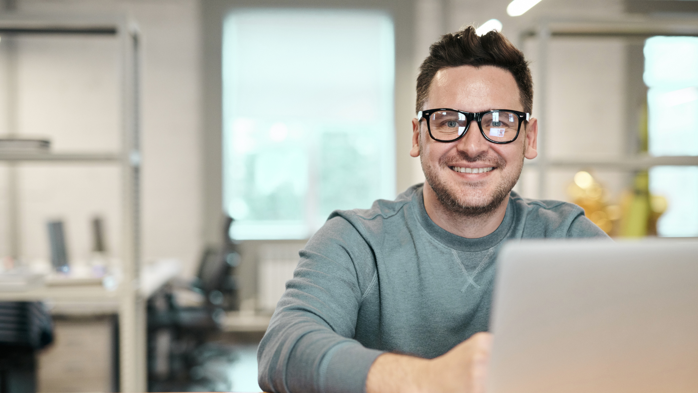 man with glasses smiling in front of his laptop